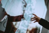 A person touching his image reflecting on a glass